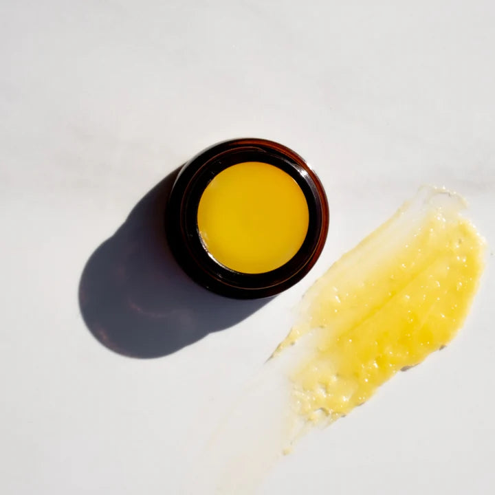 gold colored lip butter in small amber jar and a swipe of the lip butter next to it