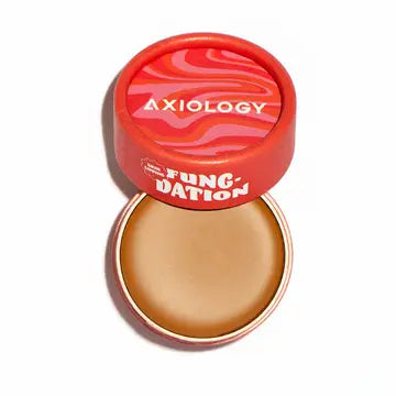 A round container of Axiology Fungdation Mushroom Foundation with a red, wavy-patterned lid, partially open to reveal the beige balm inside. The brand name "Axiology" is displayed on the lid.