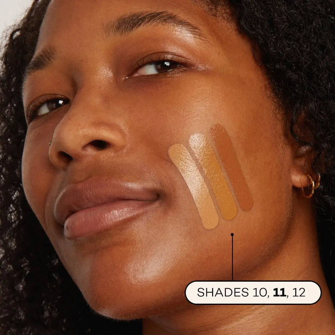 Close-up of a woman’s face with three Axiology Fungdation Mushroom Foundation swatches—shades 10, 11, and 12—on medium-brown skin. The satin finish shades are labeled and clearly show distinct color differences.