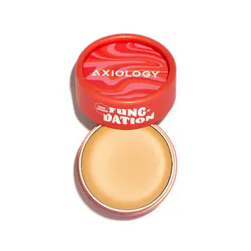 A round, open red container holds hydrating Fungdation Mushroom Foundation. The angled lid features the Axiology brand name and "Fungdation" in bold white on a red and pink swirled background.