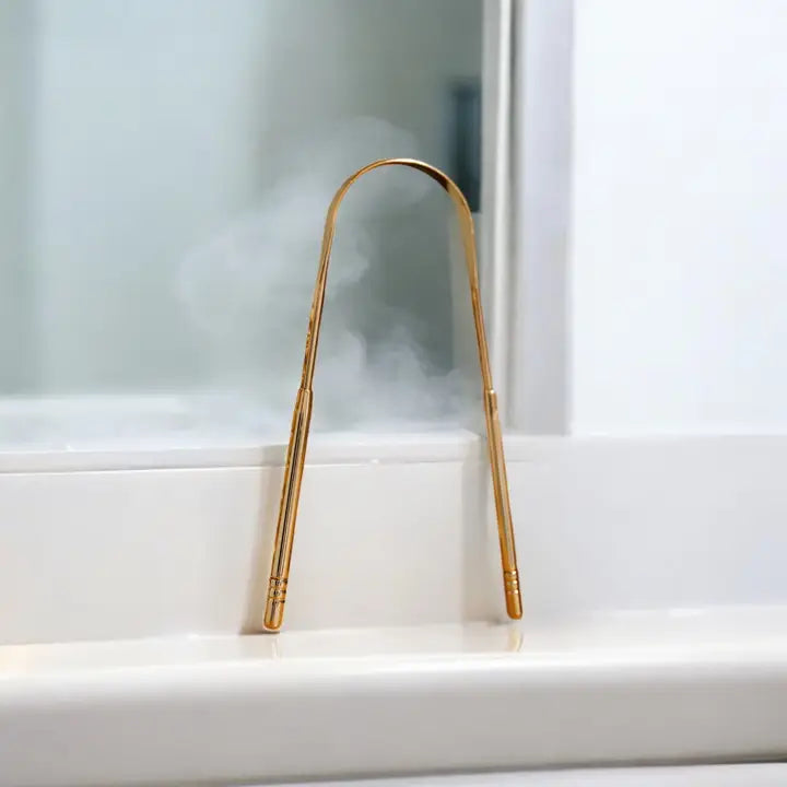 tongue scraper in gold propped up against a bathroom mirror