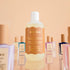 bkind nail polish remover in a clear plastic bottle and rust colored design floating in front of nail polishes of various colors