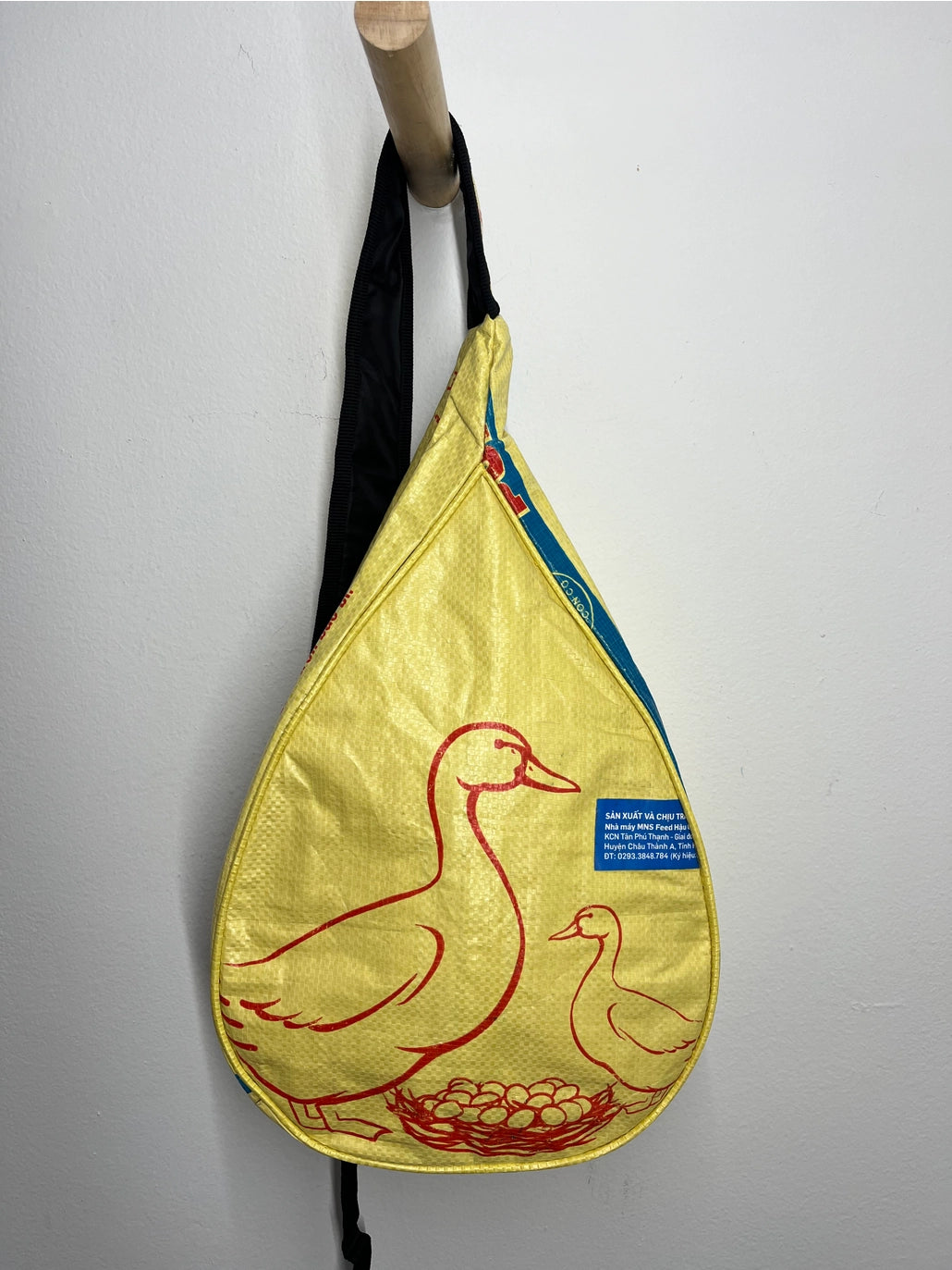 Yellow sling bag with duck design hanging on a white wall