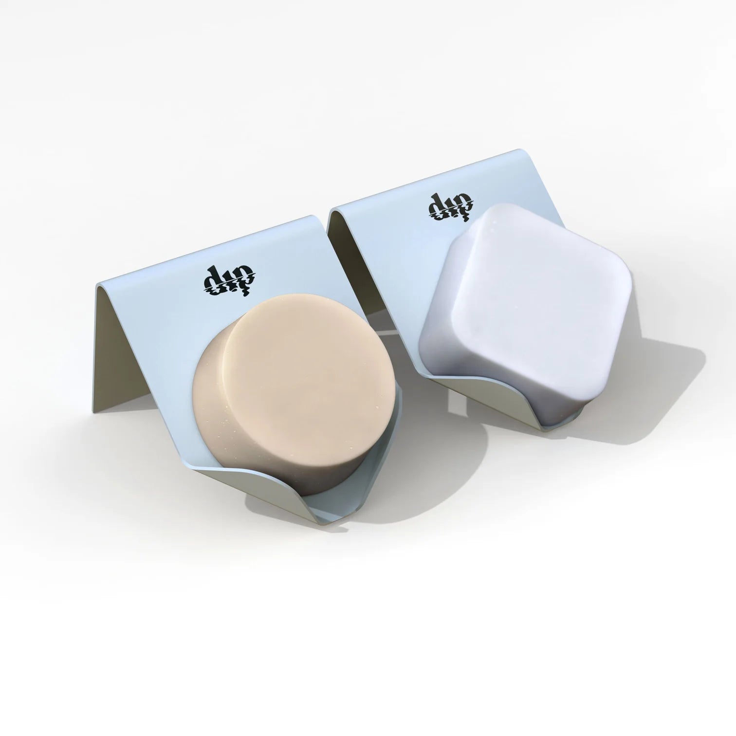 Two Life Preserver Draining Soap Dishes from Dip, made of durable metal, sit on a white surface—one cradling a round beige soap, the other a square white bar. An eco-friendly solution for neat soap organization.