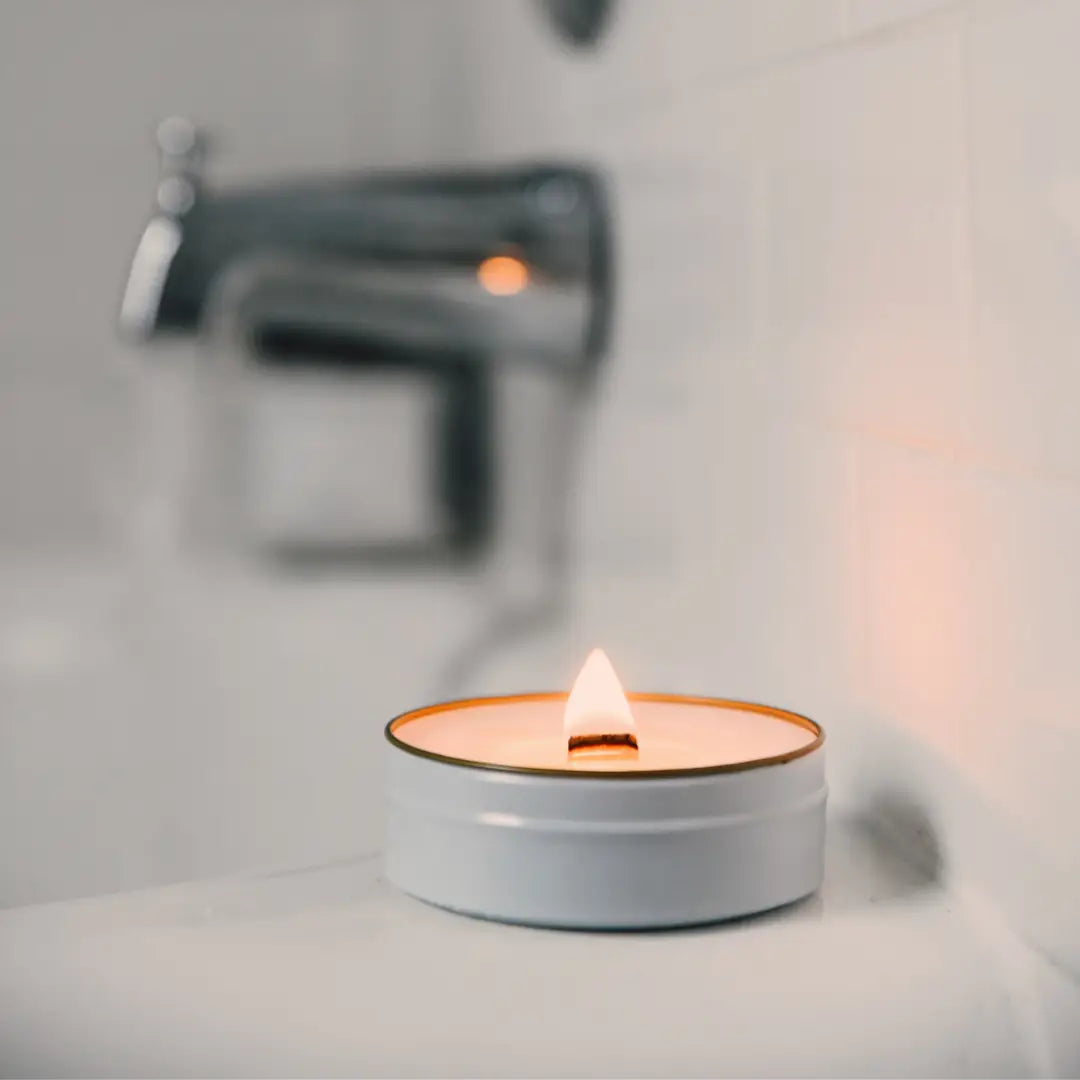 Candle in a white tin on a bathroom counter with blurred background