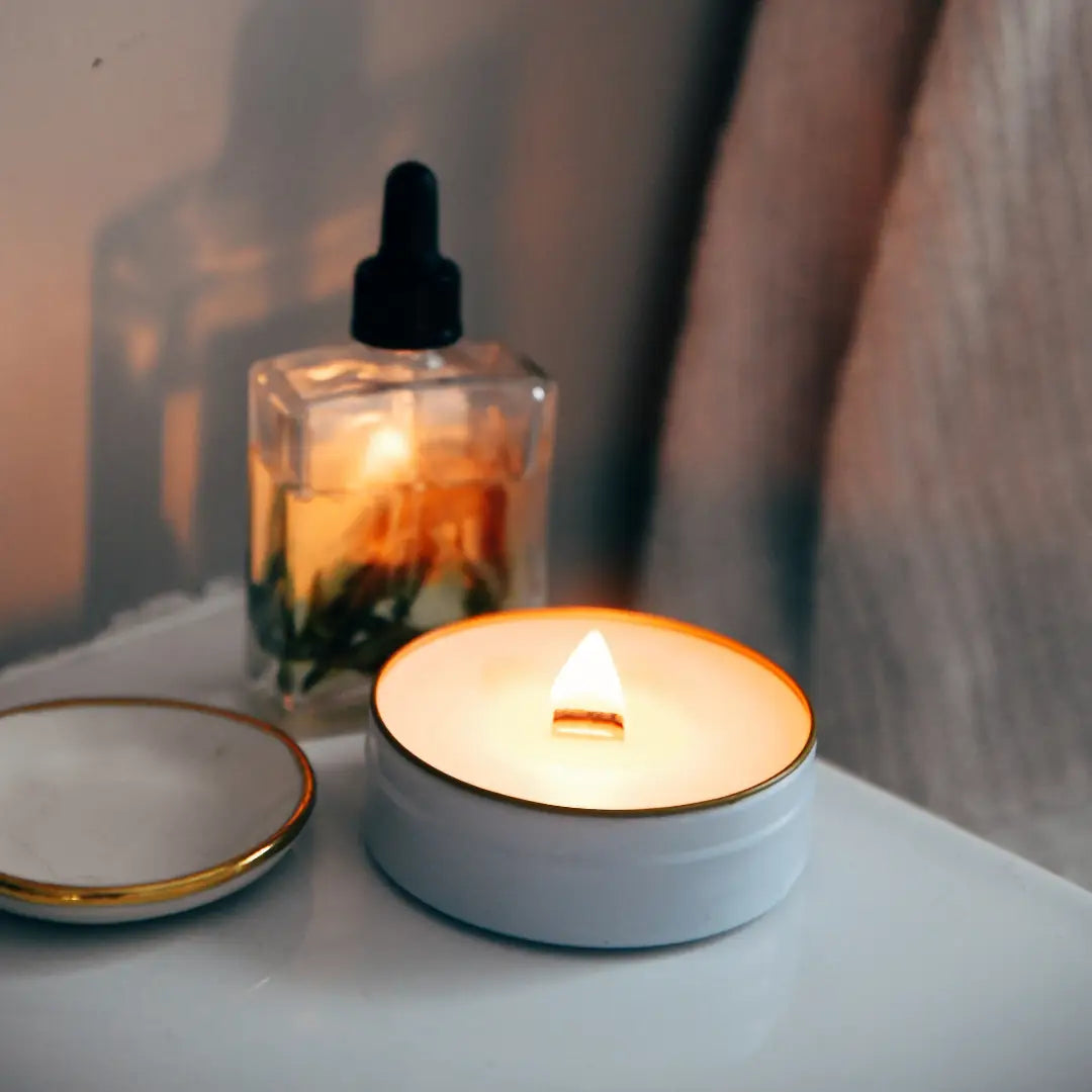 Candle in a tin with a dropper bottle in the background on a neutral surface