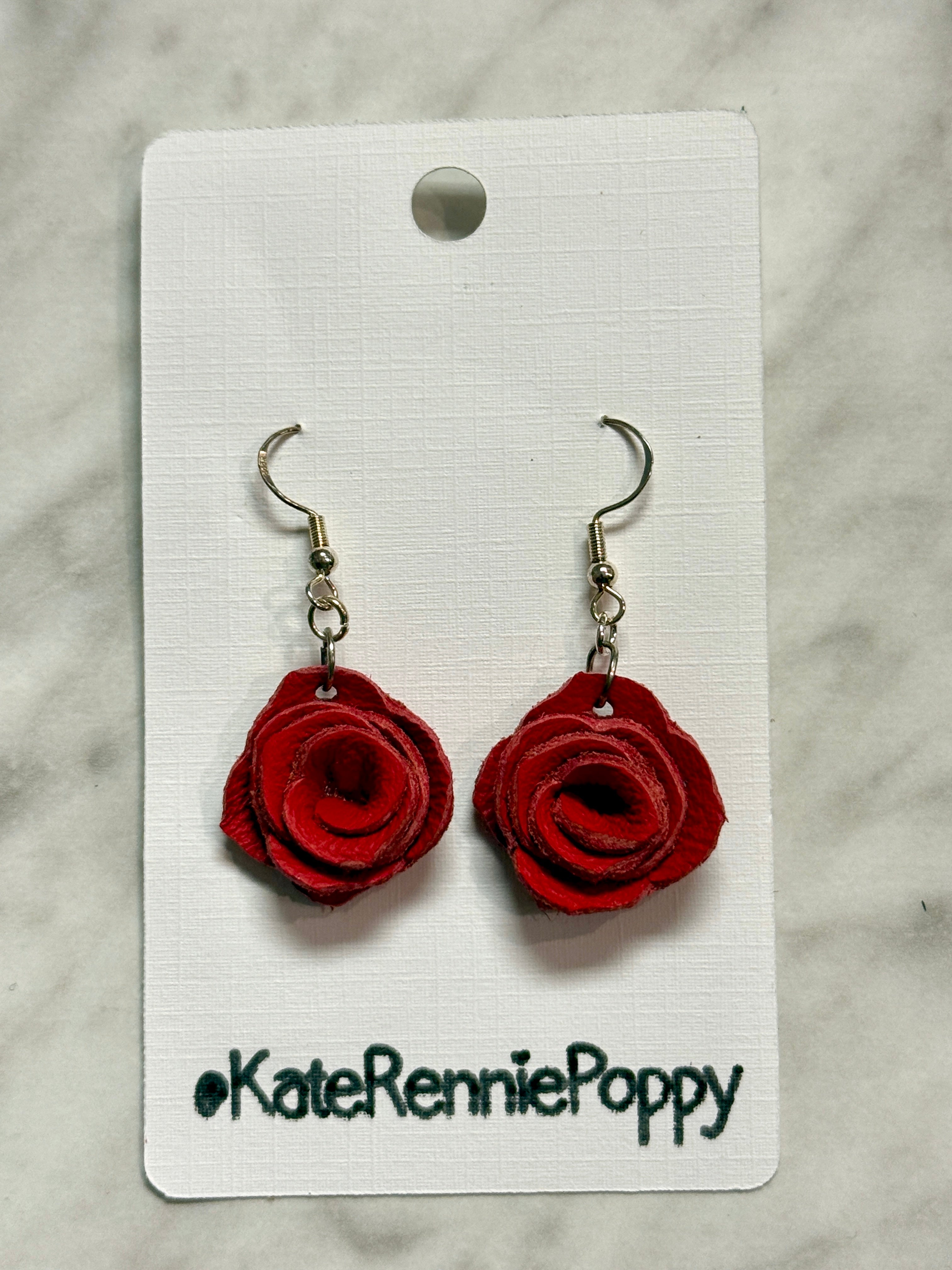 Red rose-shaped earrings on a white card with &
