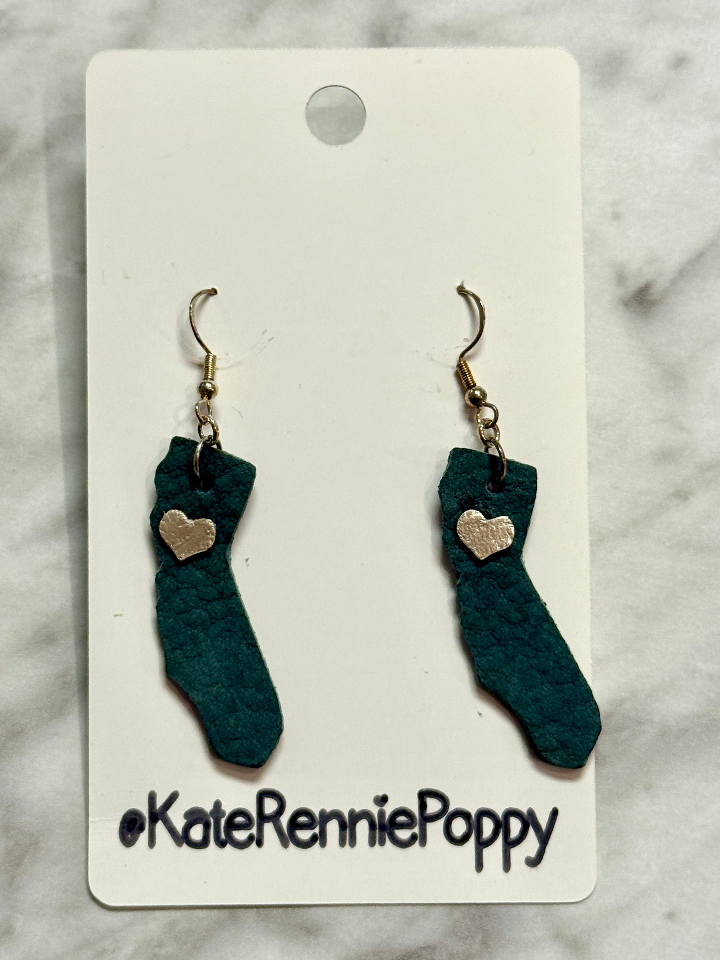 Sock-shaped earrings with heart details on a Kate Rennie Poppy card against a marble background.