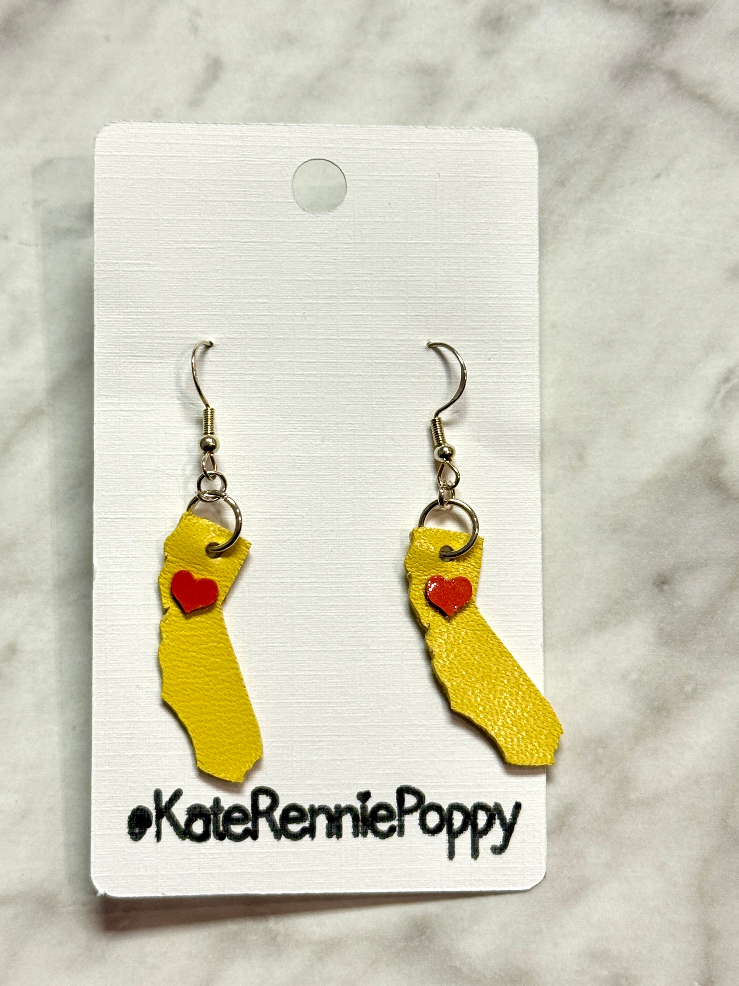 Yellow sock-shaped earrings with red hearts on a white card labeled &