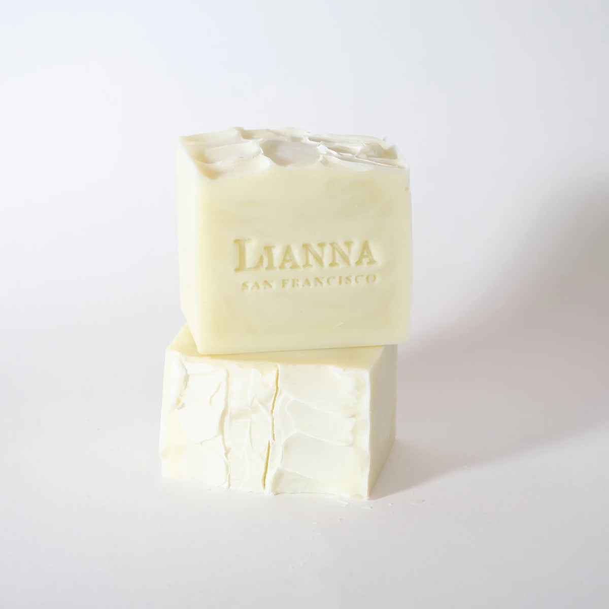Two off-white bars of Lianna Solid Dish Soap are stacked against a white background. The upper bar features the LIANNA SAN FRANCISCO engraving, and the lower bar displays a natural, textured surface. This solid, plastic-free dish soap by Lianna delivers both eco-friendly performance and refined style to your kitchen routine.
