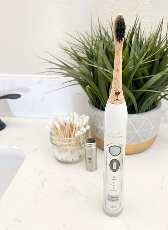 Electric toothbrush with bamboo handle on a bathroom counter next to a plant and other items.