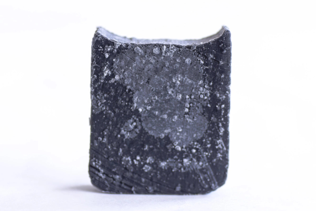 A close-up of the No Tox Life Solidsilk® Onyx Facial Cleansing Bar—a rectangular, black bar with rough texture and white specks—standing upright against a white background. A vegan, zero-waste face cleanser option.