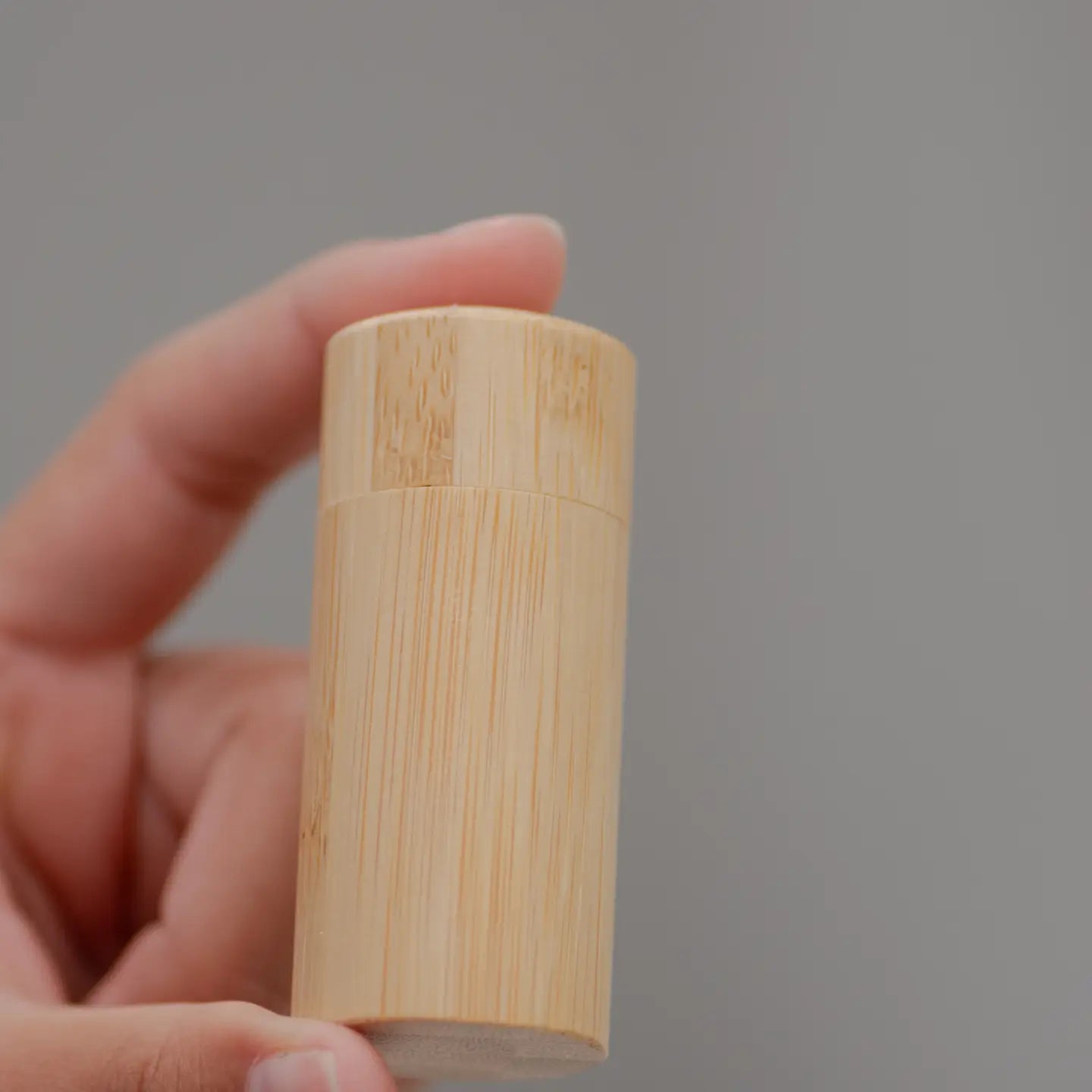 Hand holding a cylindrical wooden object against a gray background