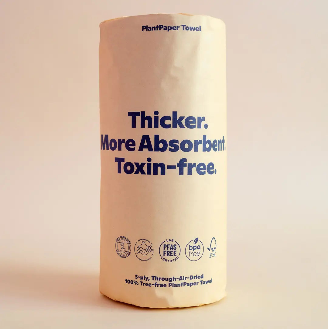 A roll of Plant Paper Towels by Plant Paper, unbleached with beige packaging and bold blue text: Thicker. More Absorbent. Toxin-free. Eco-friendly icons and certifications are displayed at the bottom of the pack.