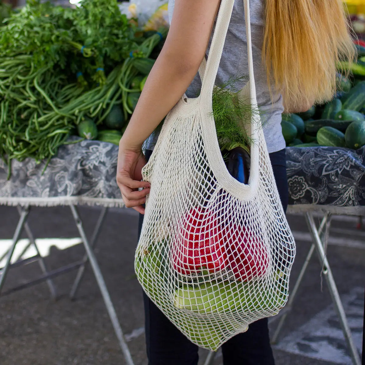 Person holding a string bag filled with groceries at an outdoor market.
