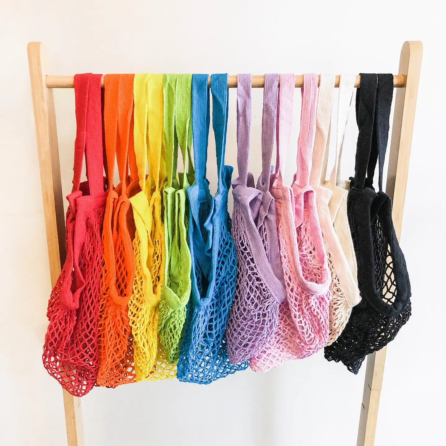 Set of colorful mesh bags on a wooden rack against a white background