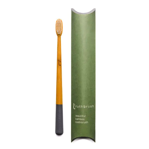 The Truthbrush - Bamboo Toothbrush by Truthbrush stands upright with light bristles and a dark grey base beside its green packaging labeled as a beautiful bamboo toothbrush.