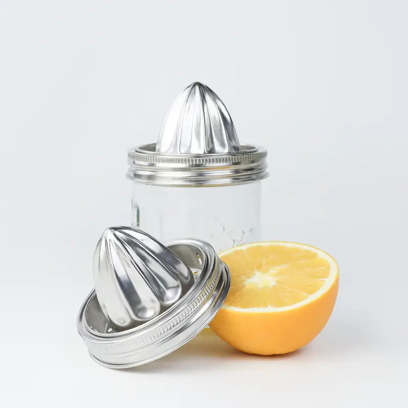 Glass citrus juicer with metal reamer and half a lemon on a white background