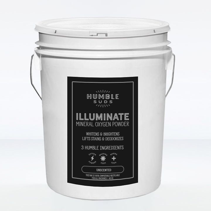A white bucket with metal handles features a black label reading Humble Suds Bulk Illuminate - Mineral + Oxygen Powder: a multipurpose cleaner that whitens, brightens, lifts stains, and deodorizes using just 3 simple ingredients.