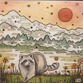 A raccoon stands in grass near orange flowers with a river, pine trees, and snowy mountains behind under an orange sky—art by Fay Helfer. Perfect for local artist cards: Artist Fay Helfer Greeting Cards by Fay Helfer.