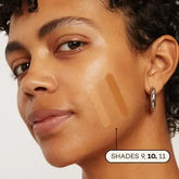 A person with glowing skin shows three swatches of Axiology Fungdation Mushroom Foundation in shades 9, 10, and 11 on their cheek. Shade 10 is bolded. They are also wearing a silver hoop earring.