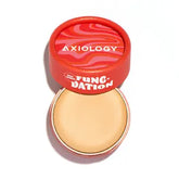 A round, red container labeled "Axiology Fungdation Mushroom Foundation" sits with its wavy red and pink lid partially open, showing the beige satin-finish foundation inside, enriched with gentle mushroom ingredients.