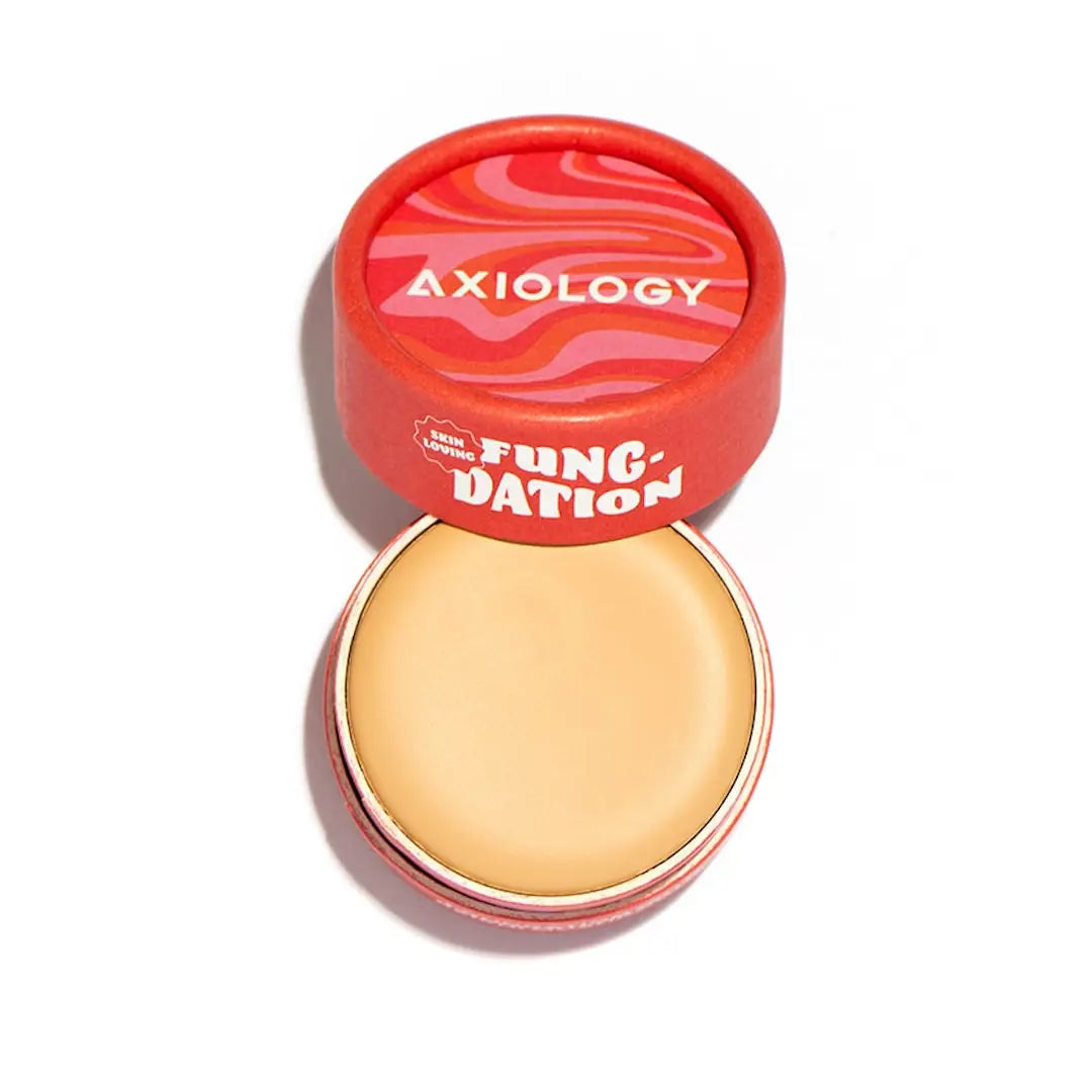 A round, open container of Axiology Fungdation Mushroom Foundation with a swirled red and pink lid resting above the beige product inside, photographed on a white background.