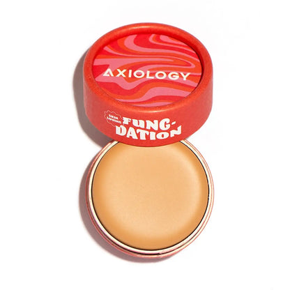 A round tin of Axiology Fungdation Mushroom Foundation with a red lid, brand name, and colorful wavy pattern is shown open to display the light beige foundation inside.