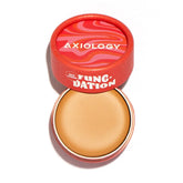 An open round container with a red lid labeled Axiology Fungdation Mushroom Foundation reveals beige hydrating foundation inside. The bold packaging showcases wavy red and pink designs.