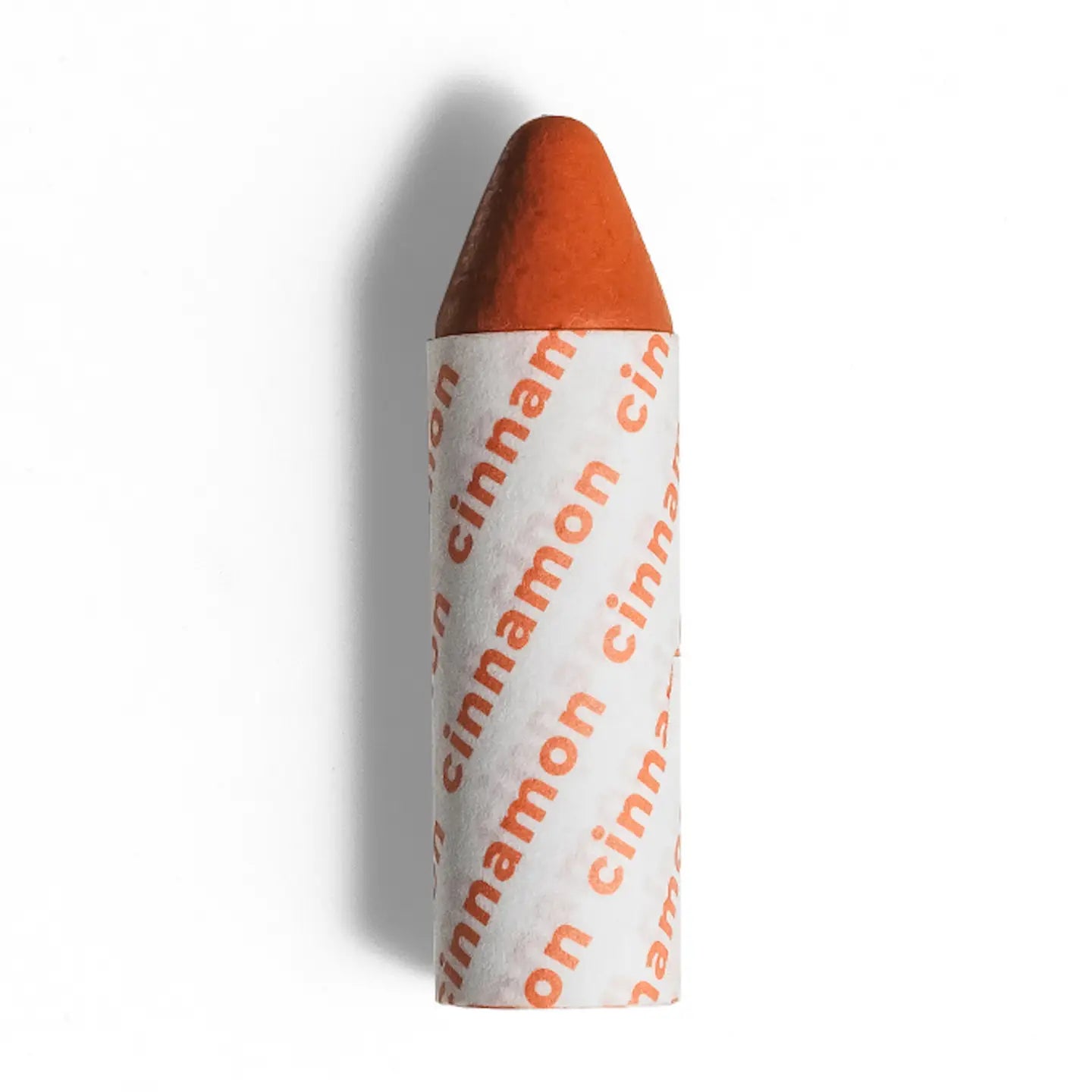 Axiology’s 3-in-1 Balmie Crayon Singles: a cylindrical orange crayon-shaped balm with one pointed end, partially wrapped in white paper printed with “cinnamon”—resembling a multi-use crayon with zero waste packaging. 