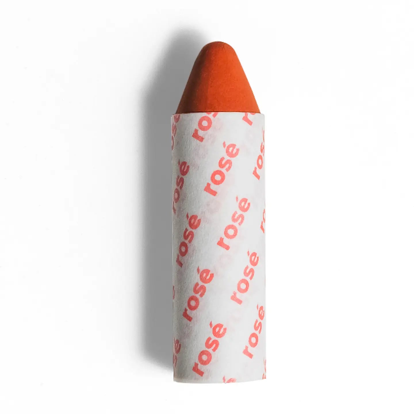 Axiology’s 3-in-1 Balmie Crayon Single in a short, orange stick partially wrapped in white paper printed with ”rosé” in pink—a perfect plastic-free choice for eco-conscious makeup lovers. 