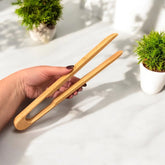 Hand holding wooden tongs on a light surface with plants in the background