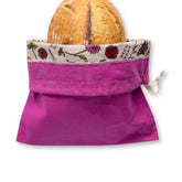 Purple reusable bread bag with floral trim holding a loaf of bread on a white background