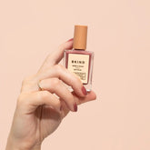 Hand holding a BKIND perfume bottle against a beige background