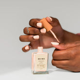 bottle of bkind nail polish in french pink with hands painting nails