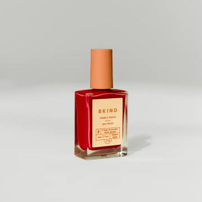 A BKind Nail Polish bottle by BKind, featuring a peach cap and red polish, is displayed against a light gray background. The label shows the brand name and product details.
