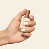 Hand holding a small bottle of nail polish with a beige background