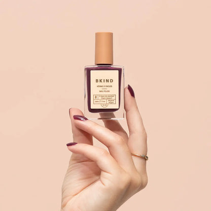 Hand holding a bottle of BKIND nail polish against a beige background