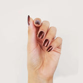 A hand with neatly manicured nails coated in shiny metallic copper BKind Nail Polish by BKind, shown against a plain white background.