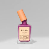 A bottle of BKind Nail Polish by BKind features a purple shade, peach-angled cap, and beige label with plant-based details, set against a plain gray background.