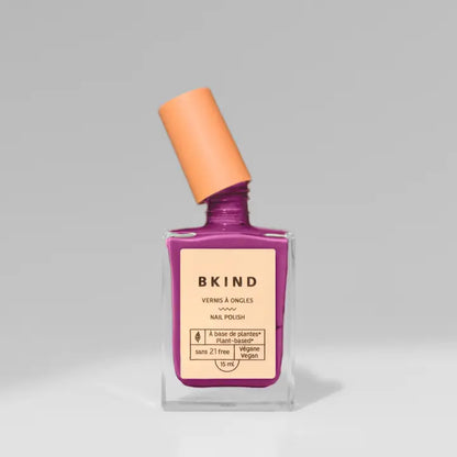 A bottle of BKind Nail Polish by BKind features a purple shade, peach-angled cap, and beige label with plant-based details, set against a plain gray background.