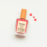 A bottle of BKind Nail Polish by BKind, featuring a beige cap and filled with bright pink polish, is displayed on a white background with three drops of pink nail polish beside it.