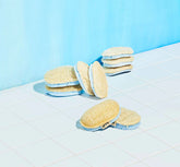 Blueland Sponges 3-pack by Blueland features several oval, plant-based sponges with beige tops and blue bottoms arranged on white tiles against a blue background—one compostable sponge includes a small fabric label.