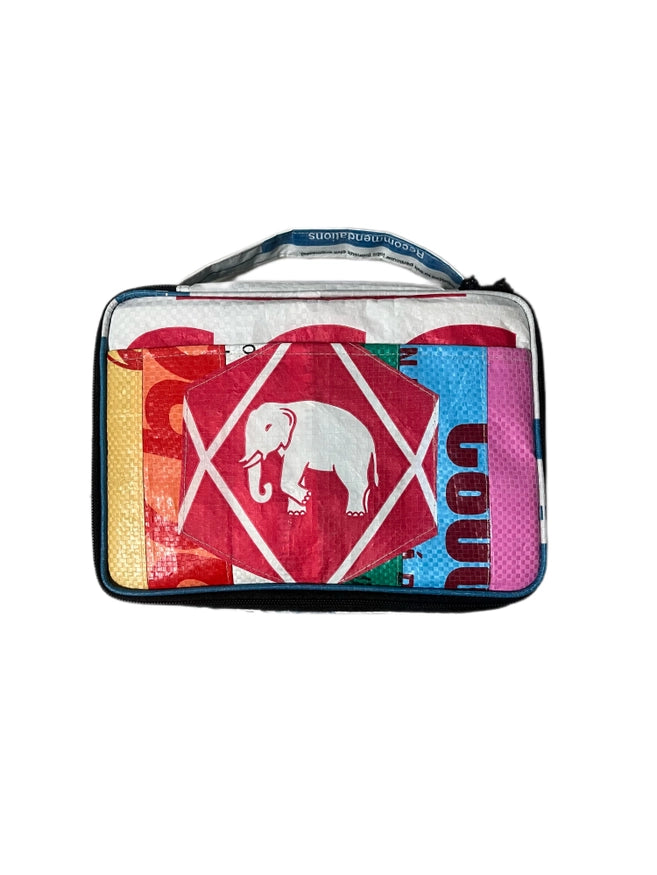 The Cement6 Lunch Box is a colorful, rectangular insulated bag with a handle, showcasing a white elephant inside a red diamond on the front and decorated with multicolored patterns and text.