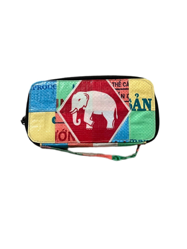 The Cement6 Zipped Clutch is a colorful, rectangular artisan bag with patchwork, a central red diamond and white elephant, green, yellow, and blue blocks. Embrace sustainable style with unique patterns and a handy wrist strap.