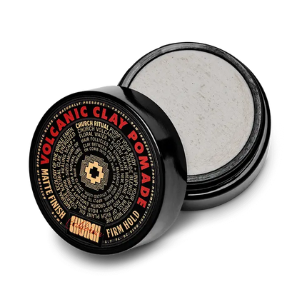 An open black container of Curch California Volcanic Clay Pomade - Firm Hold displays the product details on its lid. Inside, the light gray matte hair clay features a matte finish and firm hold, as highlighted on the label.