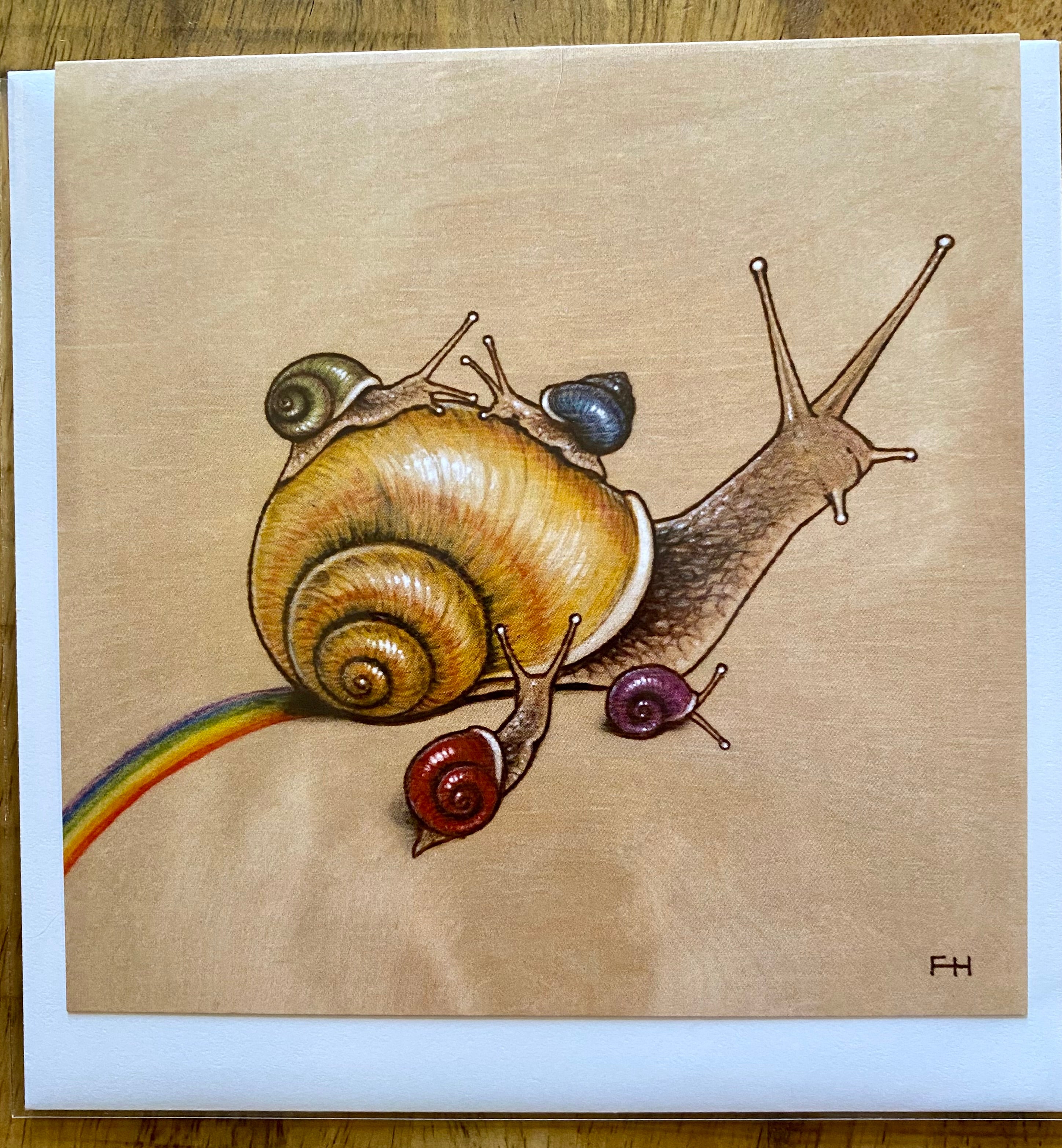 A large snail with four colorful snails on its shell and a rainbow behind is set against a beige background. FH initials in the corner represent Fay Helfer’s art, featured on Artist Fay Helfer Greeting Cards by Fay Helfer.