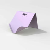 The Dip Life Preserver Draining Soap Dish, featuring a minimalist lavender curved design, rests on a white surface with "dip" printed in black on the durable stand.