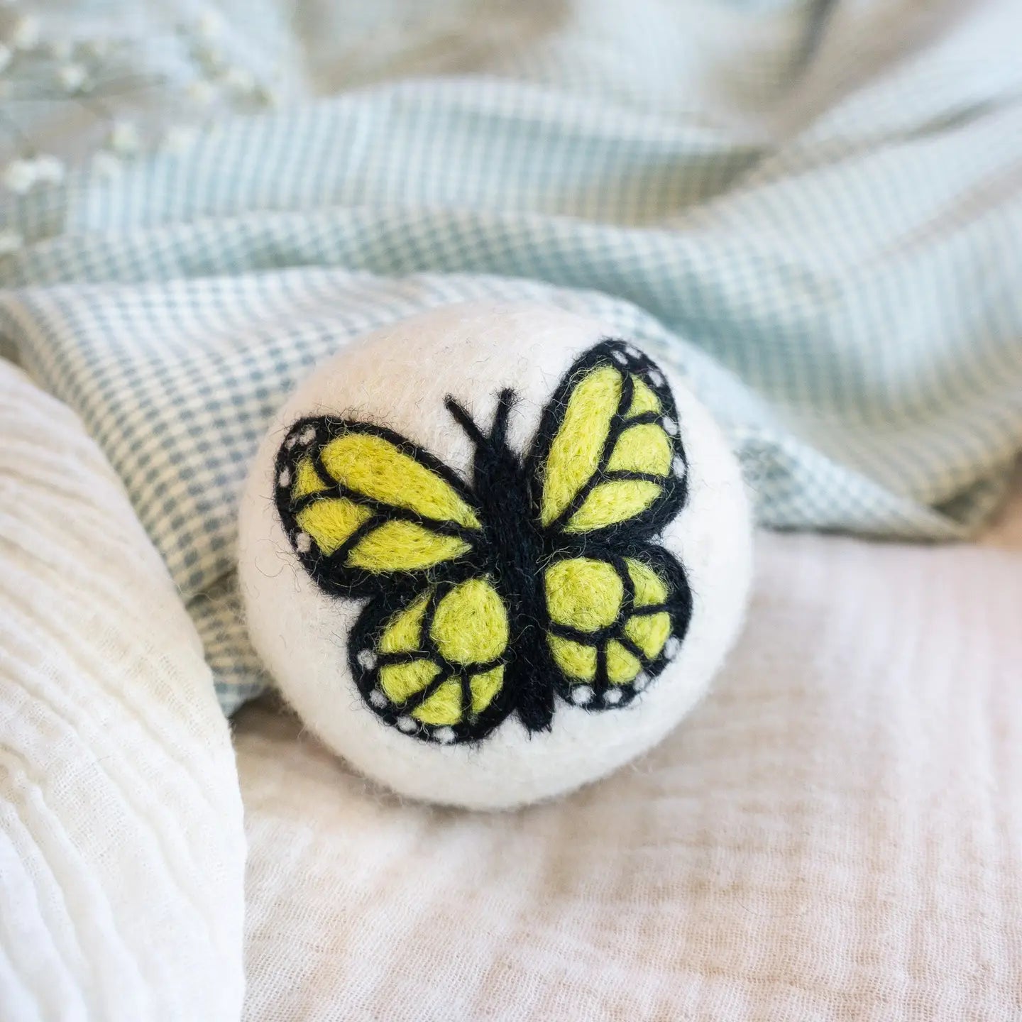 Felted wool dryer ball with a butterfly design on a textured fabric background