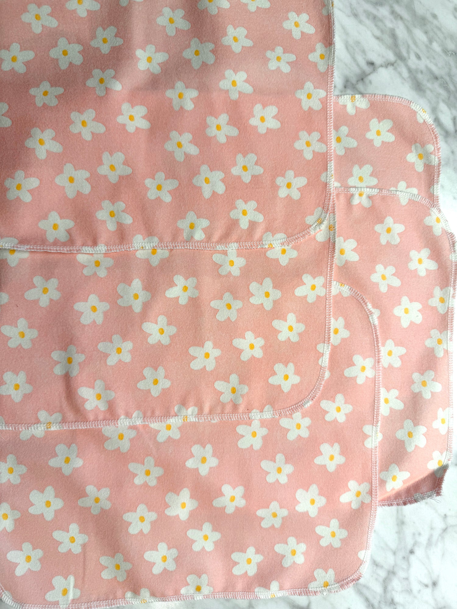 Four pink Not Paper Towels Bundles by Sustainable For Good, featuring white and yellow flower patterns, overlap on a gray marbled surface—these reusable towels are an eco-friendly alternative to single-use paper towels.